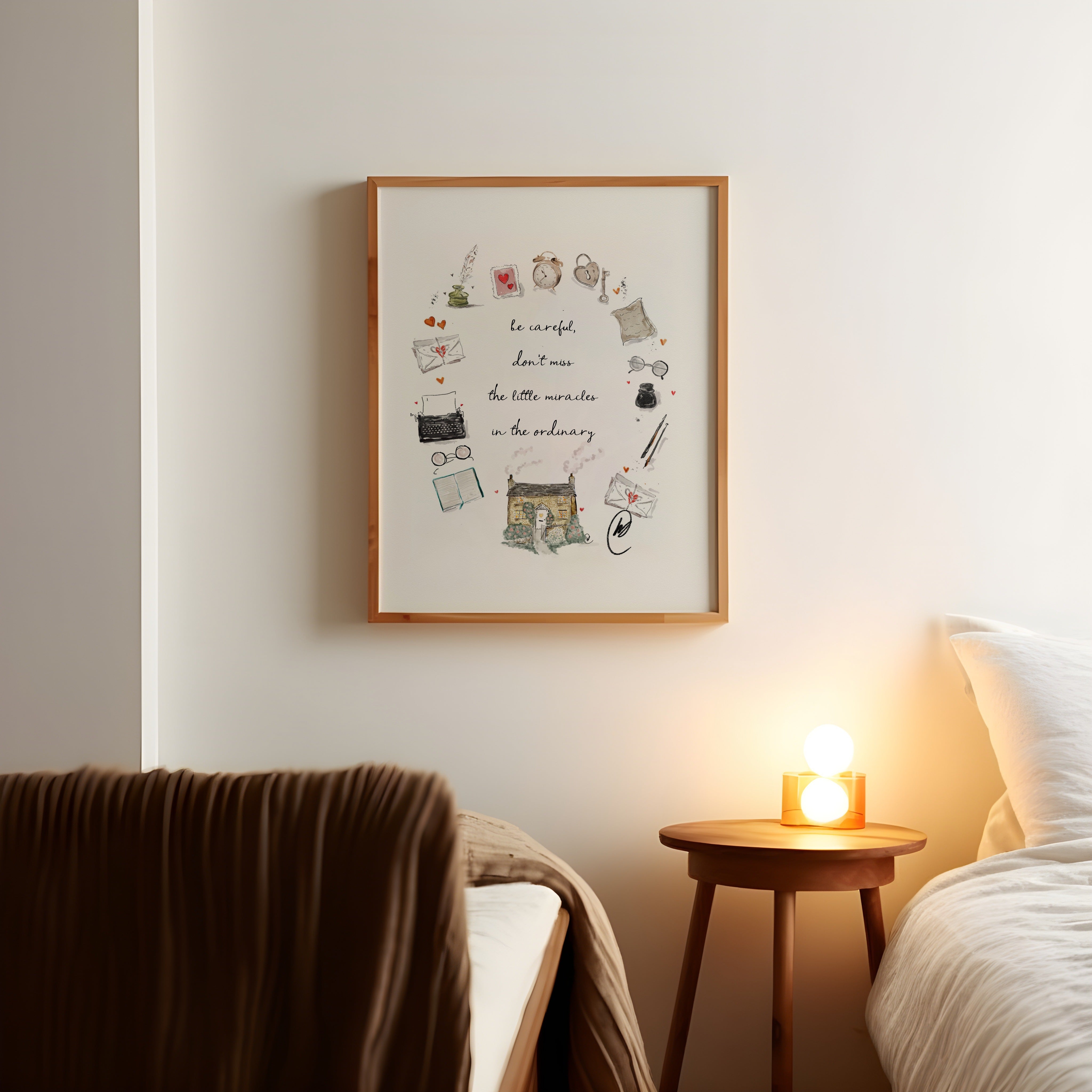 The 'be careful, don't miss the little miracles in the ordinary' cottage wreath illustration shown as a framed print in a warm oak frame, hanging on a bedroom wall above a bedside table with a lit lamp. Frame not included.