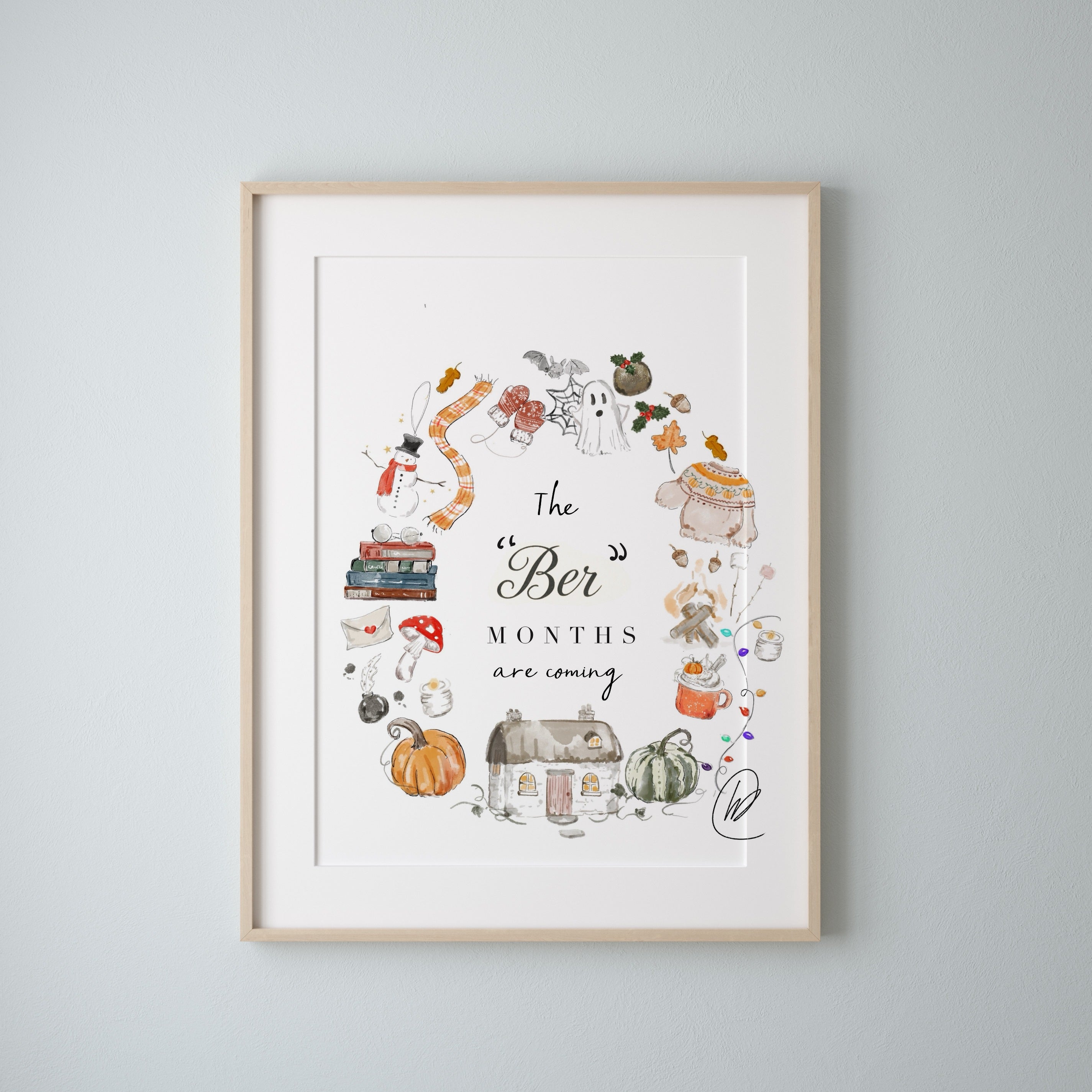 The Ber Months Are Coming print shown in a light oak frame with a white mount on a pale grey blue wall, the watercolour wreath of autumn and winter things sitting inside the mount window. Frame not included.